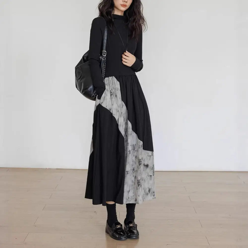 Person wearing a black and gray patterned dress with a black backpack against a white wall.