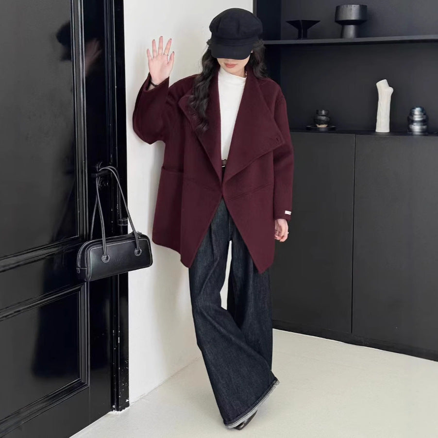 Person wearing a burgundy coat and black hat in a minimalistic room.