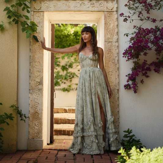 A woman standing in a doorway wearing a green floral halter dress with a floral pattern and a maxi length.