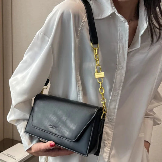 Person holding a black handbag with a gold chain strap indoors