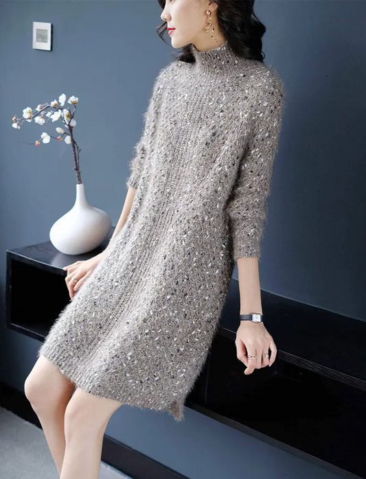 Woman wearing a silver sequin dress sitting on a black surface with a dark blue wall in the background.