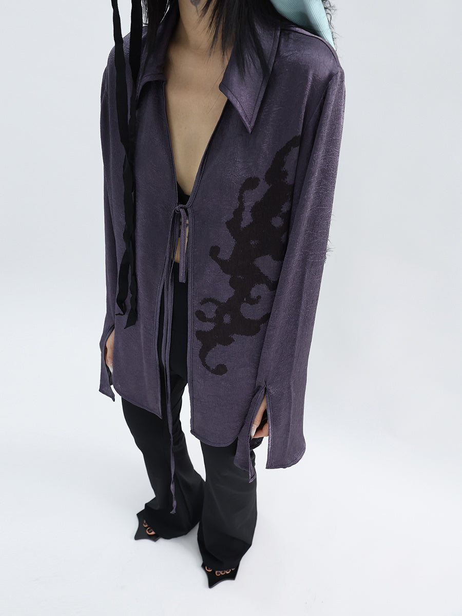Person wearing a long, dark purple cardigan with intricate black patterns on a white background