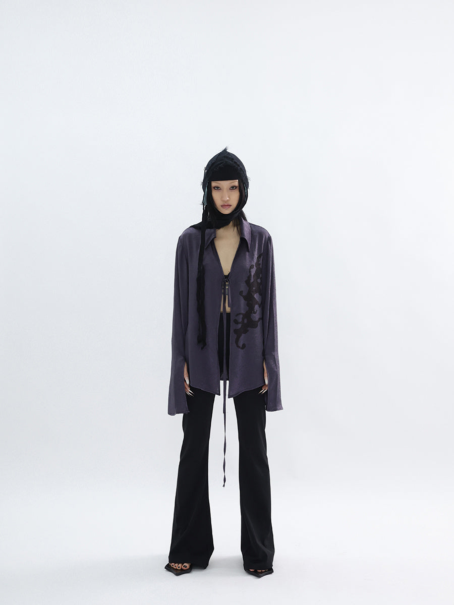 Person wearing a dark outfit with a long coat and black pants on a white background