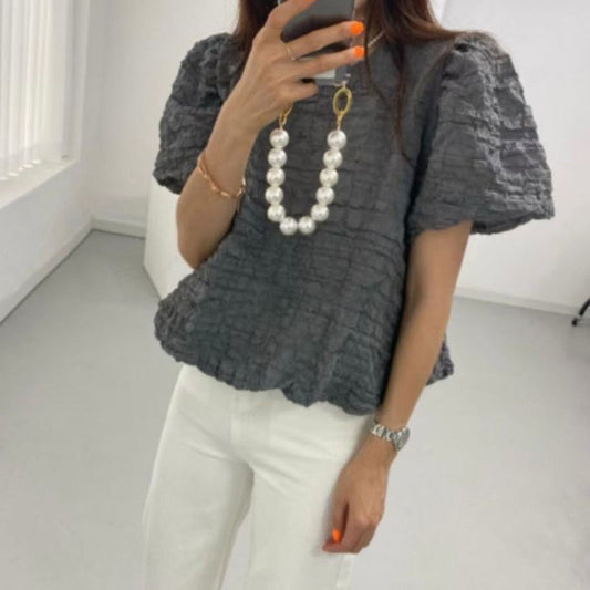 Person wearing a textured gray top and white pants in a minimalistic room.