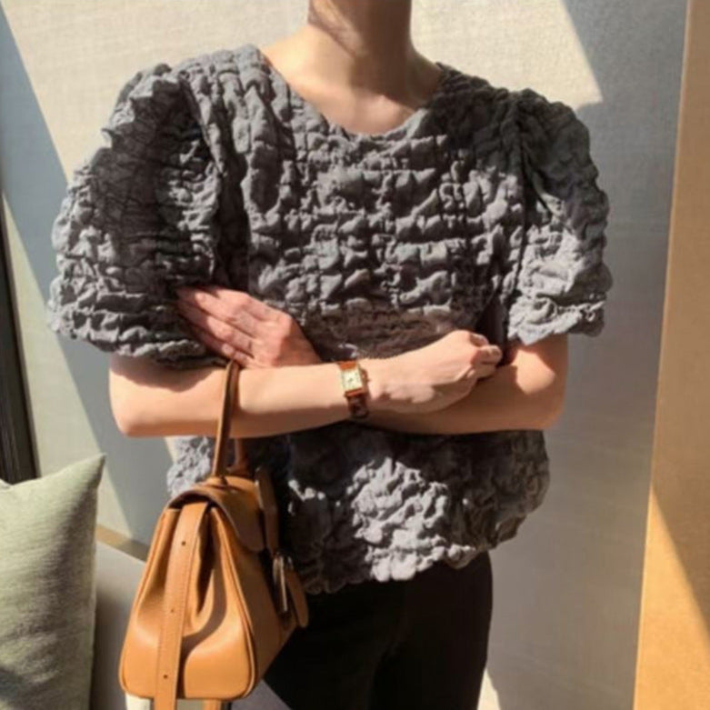 Person wearing a textured gray sweater with a brown leather bag, standing against a neutral wall.