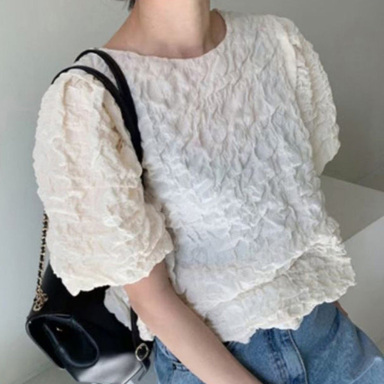 Person wearing a white textured blouse and blue jeans holding a black handbag.