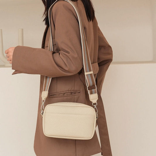 Person wearing a beige crossbody bag with a plain background