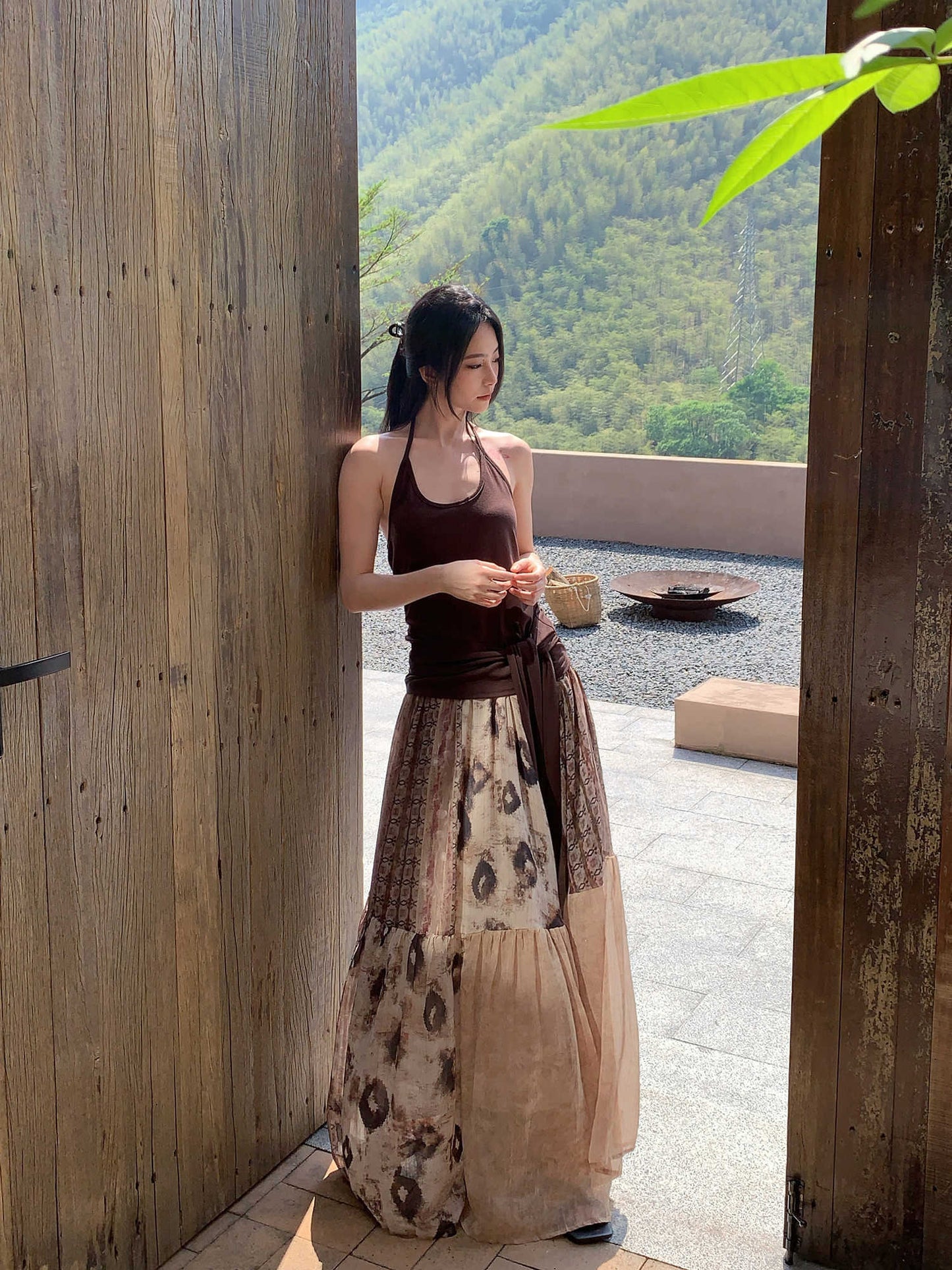 Woman in a long dress standing in a scenic outdoor setting with mountains.