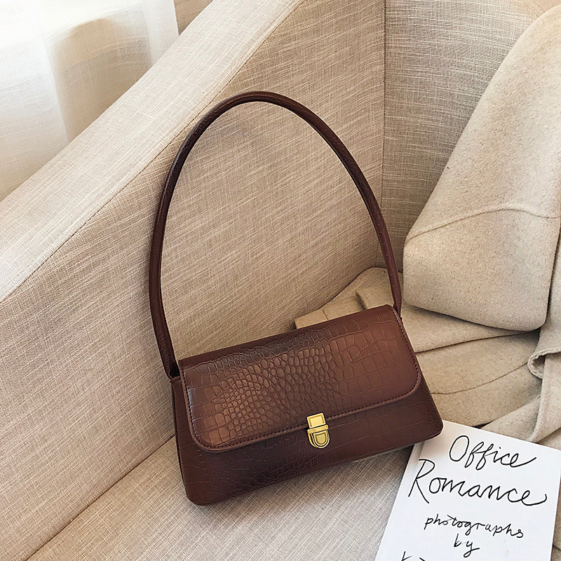 Brown handbag on a beige sofa with a book titled 'Office Romance' nearby