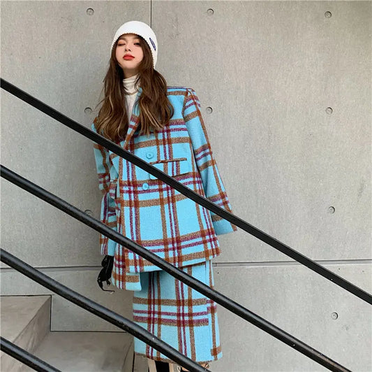 Woman wearing a blue plaid coat and skirt set against a concrete wall.