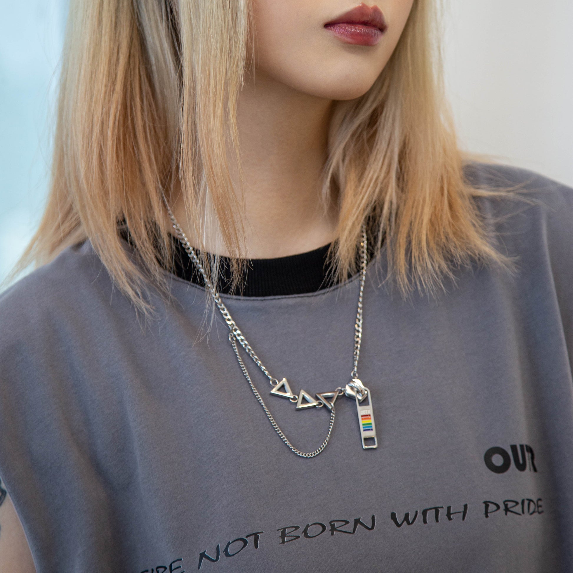 Person wearing a gray t-shirt with text and a necklace with a rainbow pendant.