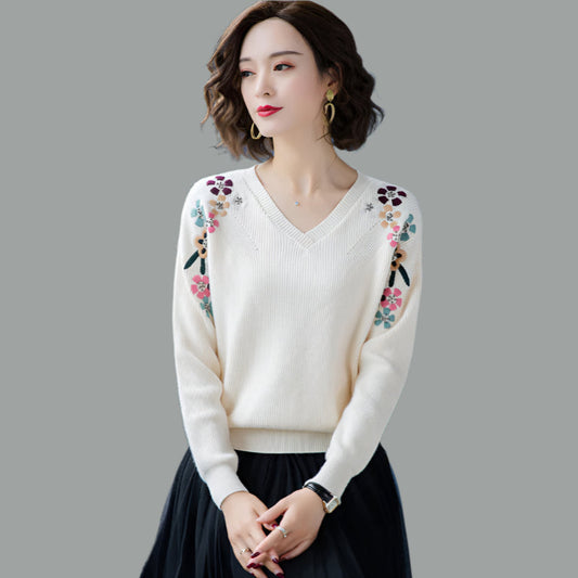 Woman wearing a white sweater with floral embroidery on a gray background