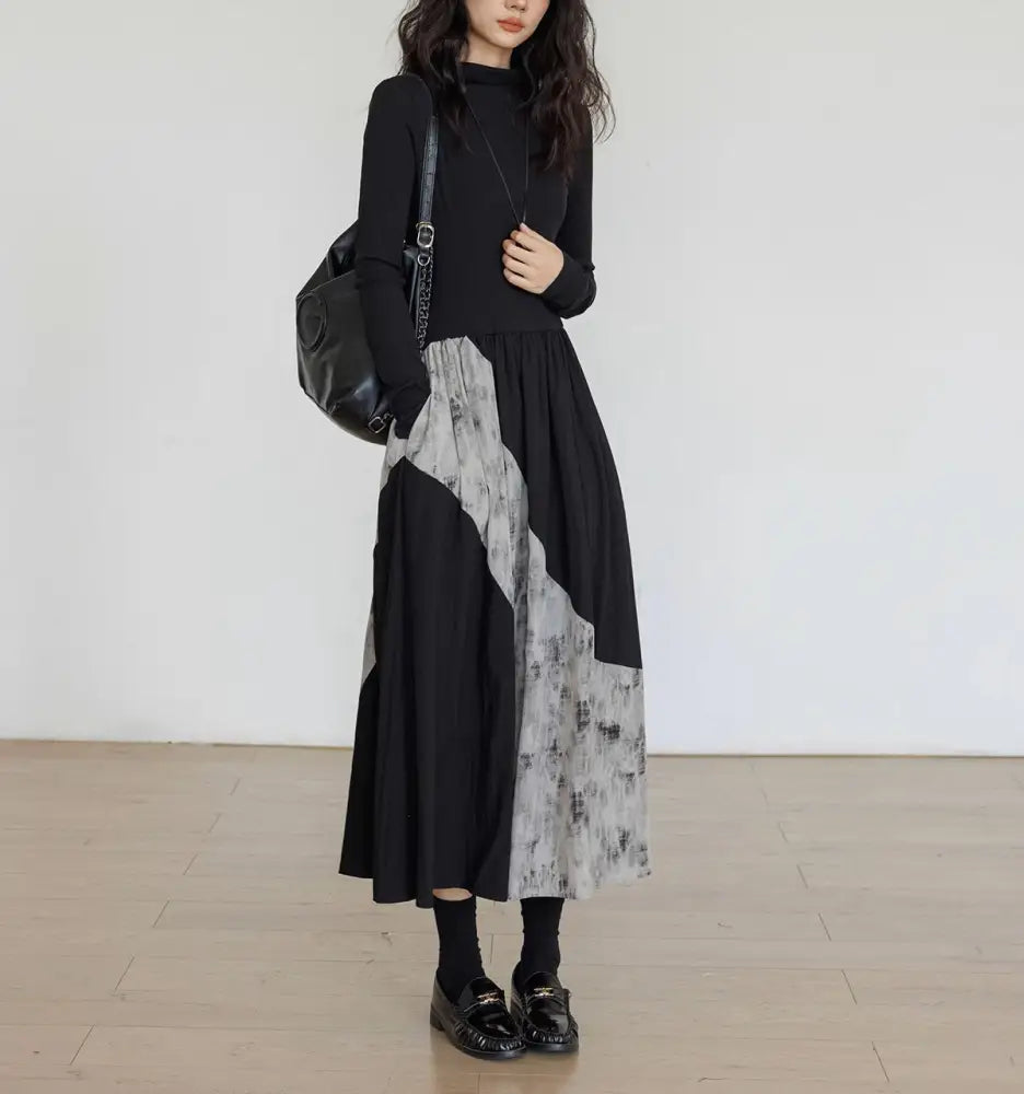 Person wearing a black and gray dress with a black bag against a white wall.