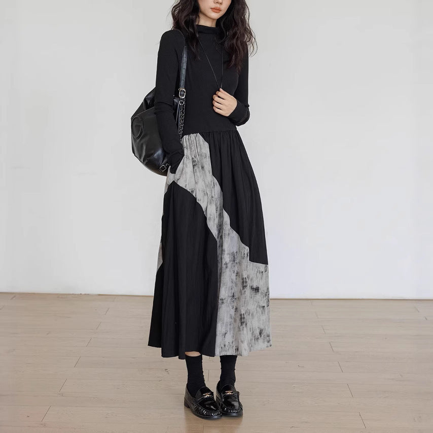 Person wearing a black and gray patterned dress with a black backpack against a white wall.