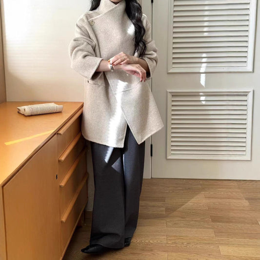 Person wearing a beige coat standing next to a wooden cabinet in a room with a radiator.