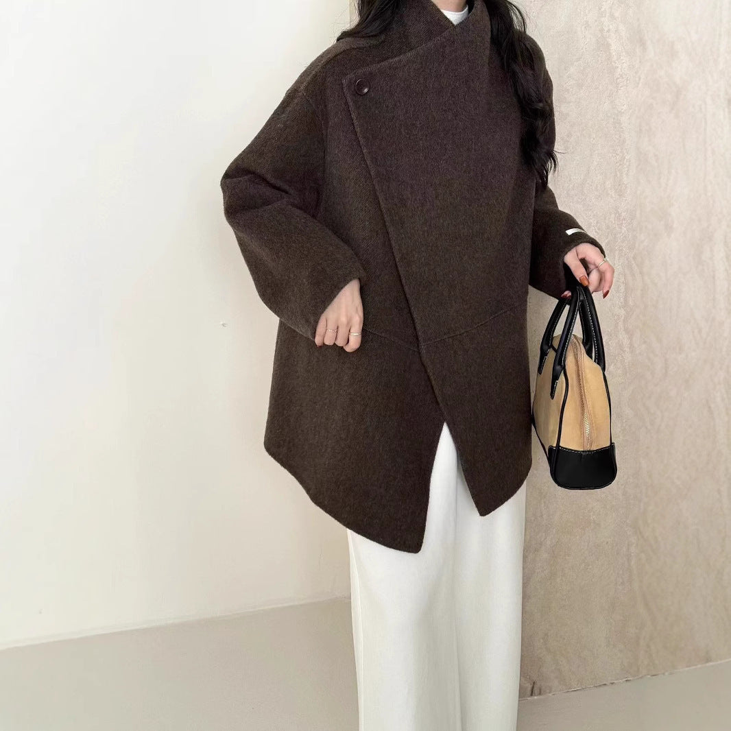 Person wearing a brown coat holding a black handbag against a neutral background