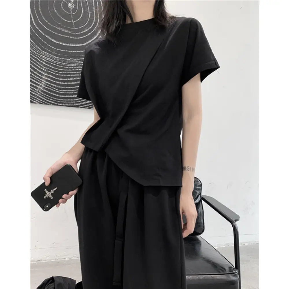 Person wearing a black outfit holding a phone and a bag against a minimal background