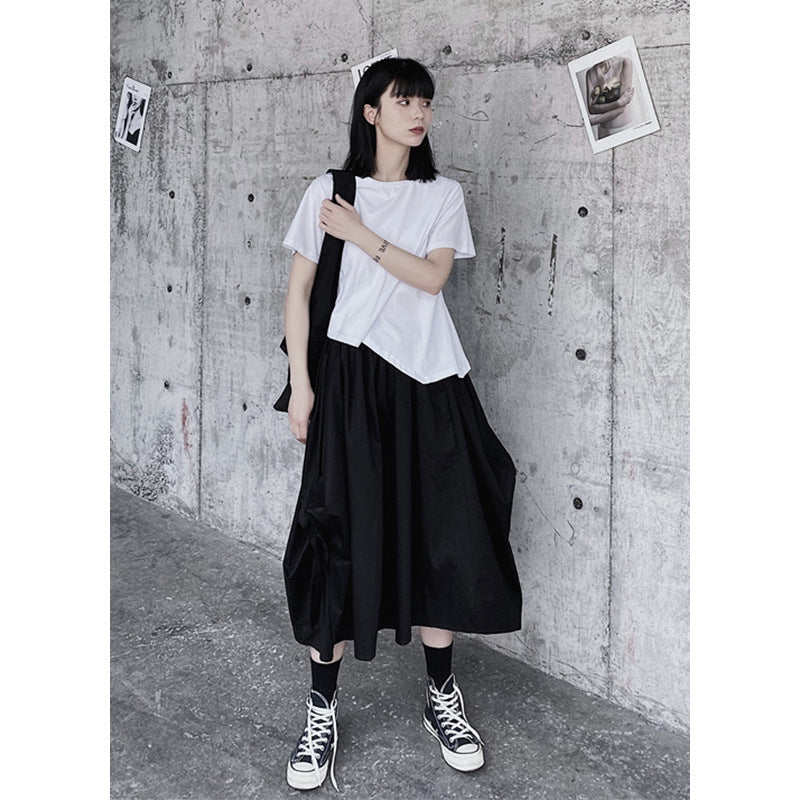 Person wearing a white t-shirt and black skirt against a concrete wall.