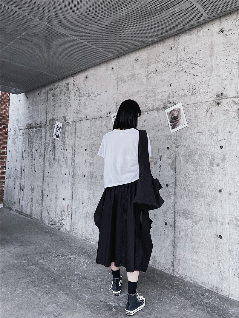 Person standing against a concrete wall with posters, wearing a white shirt and black skirt.