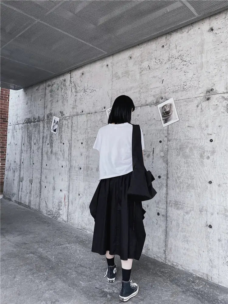 Person standing against a concrete wall with posters, wearing a white shirt and black skirt.