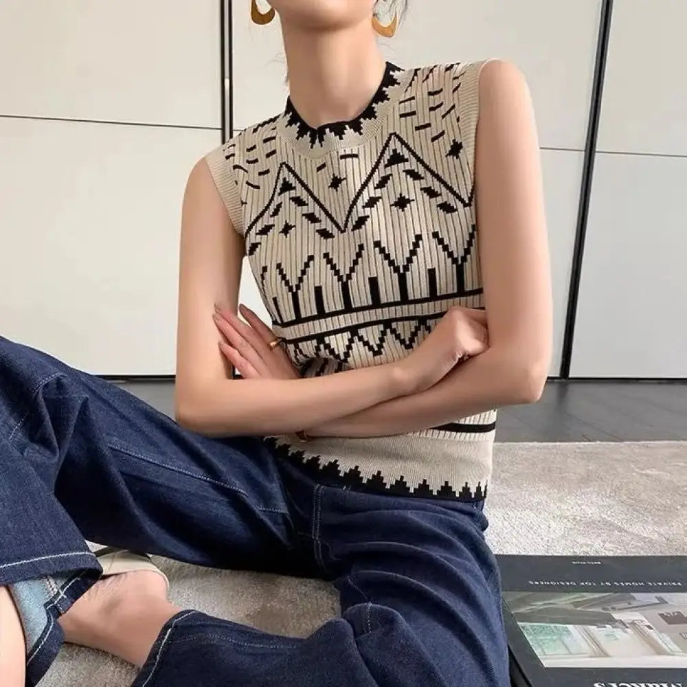 Person wearing a sleeveless patterned top and blue jeans sitting on a couch.