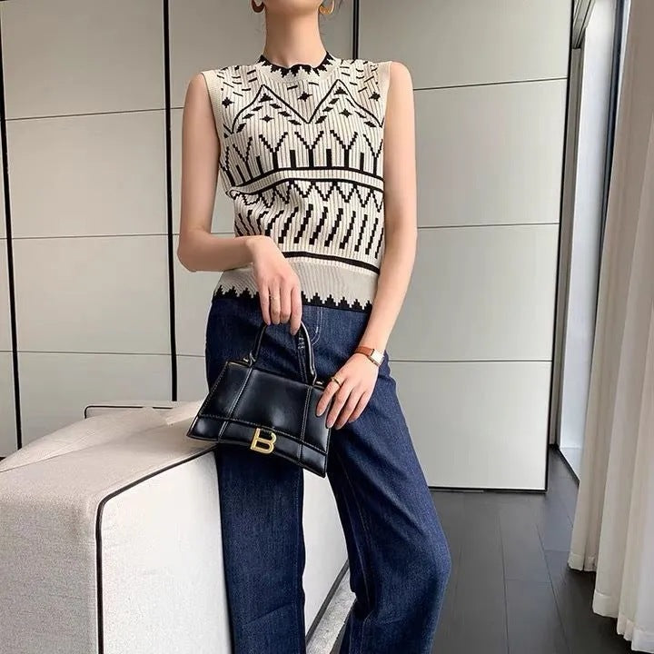 Person wearing a black and white patterned sleeveless top and blue jeans, holding a black handbag.