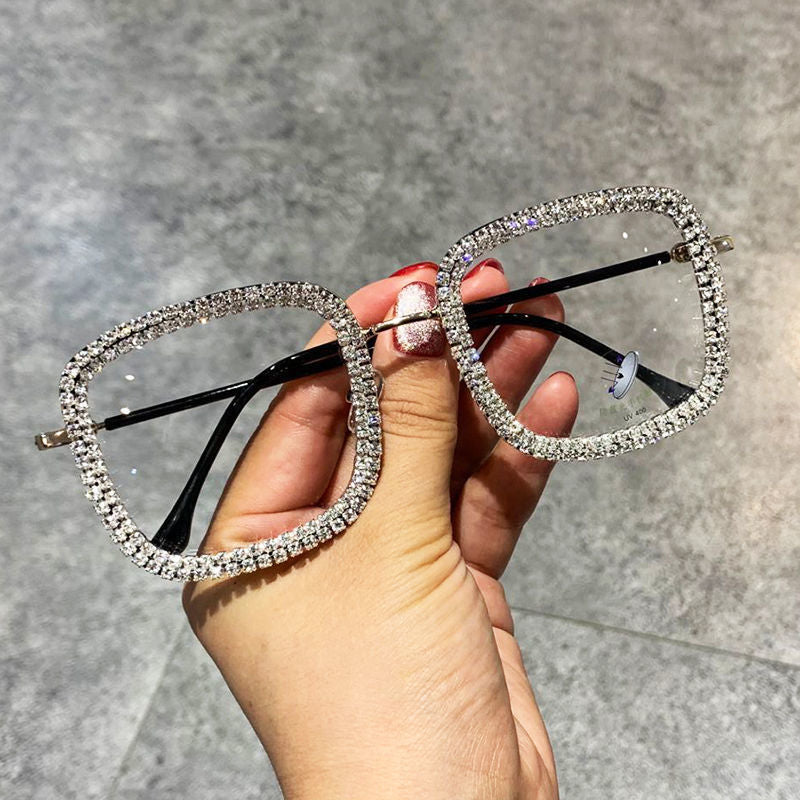 A pair of square-shaped, multicolored diamond-studded glasses with a metallic frame being held by a person with red nail polish.