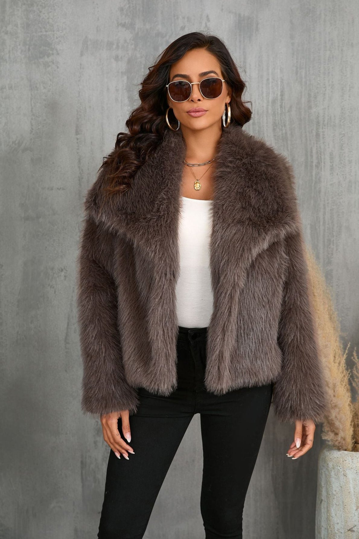 A female model wearing a large lapel fluffy plush artificial fur coat in brown color with long sleeves.