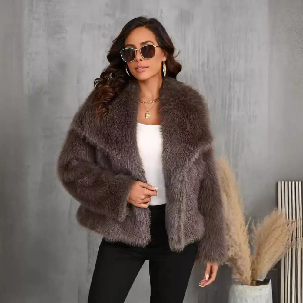 A female model wearing a large lapel fluffy plush artificial fur coat in brown color with long sleeves.