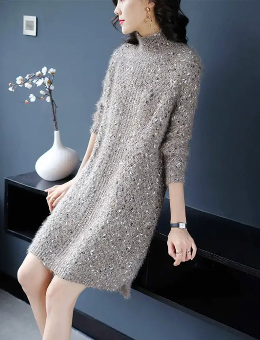Woman wearing a silver sequin dress sitting on a black surface with a dark blue wall in the background.