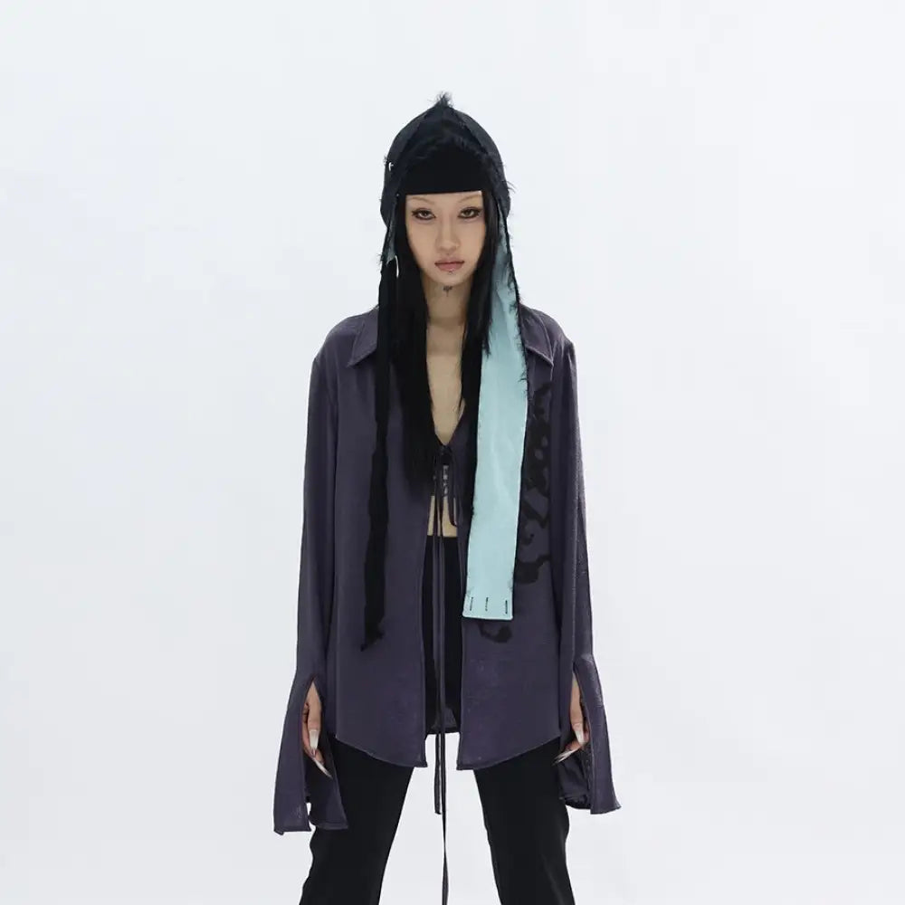 Person wearing a dark outfit with a hood and scarf on a white background