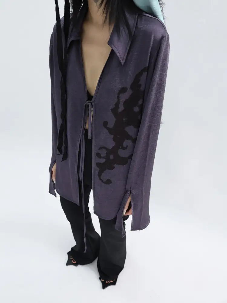 Person wearing a long, dark purple cardigan with intricate black patterns on a white background