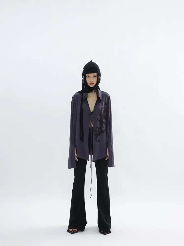 Person wearing a dark outfit with a long coat and black pants on a white background
