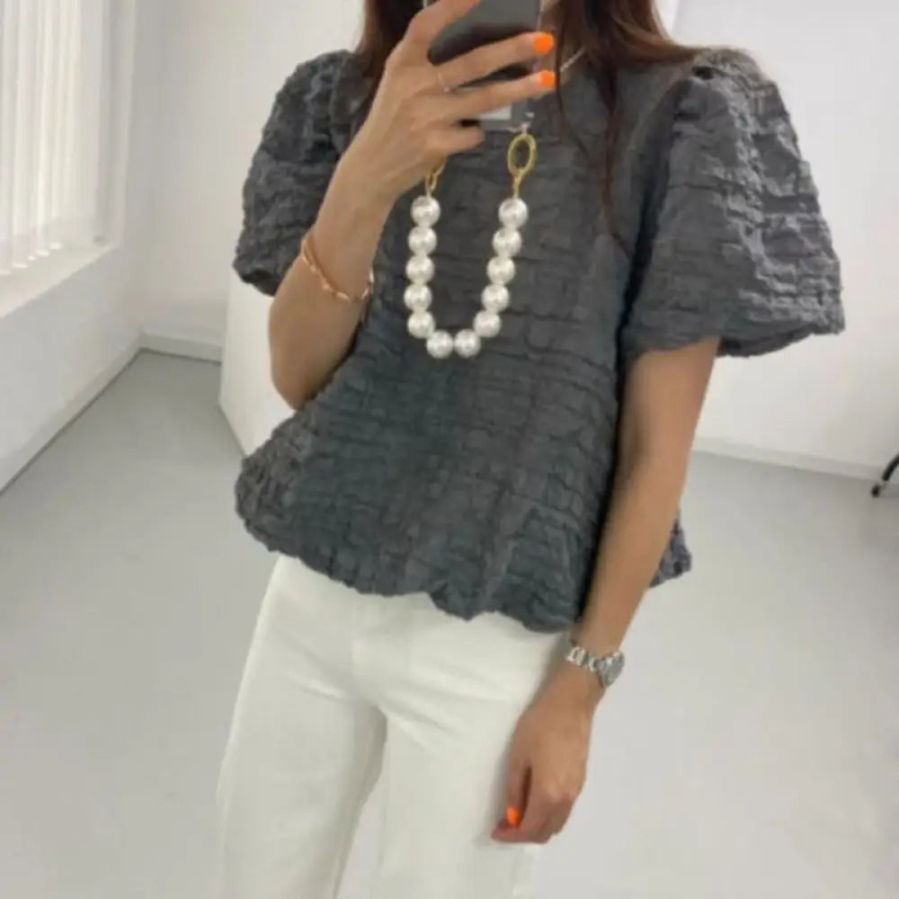 Person wearing a textured gray top and white pants in a minimalistic room.
