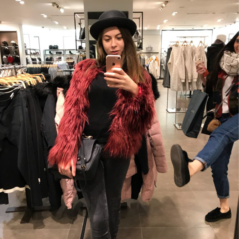 Woman taking a mirror selfie in a clothing store wearing a red fur vest and black hat.