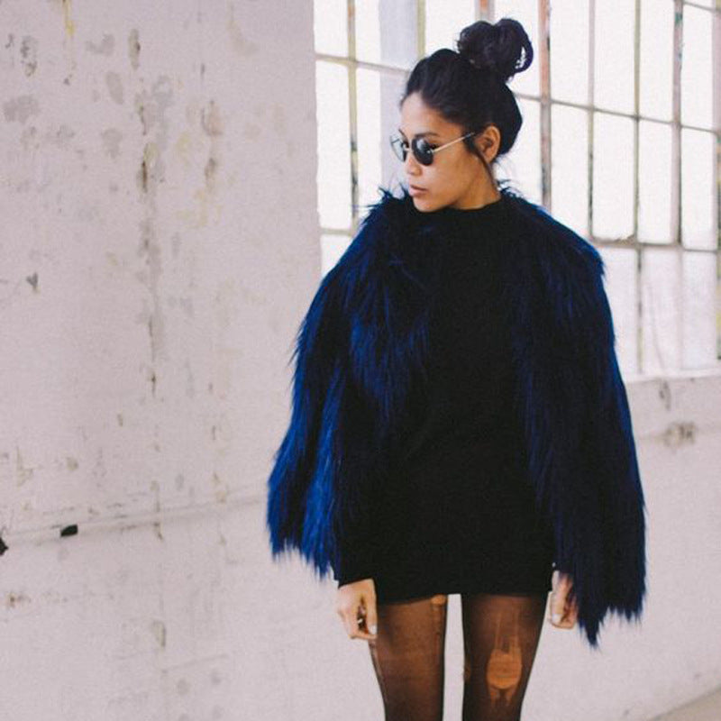 Person wearing a blue fur coat over a black outfit in an urban setting