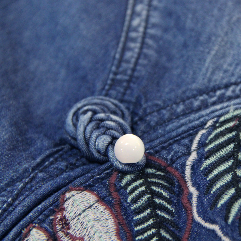 Close-up of a blue denim fabric with embroidered details and a white button.