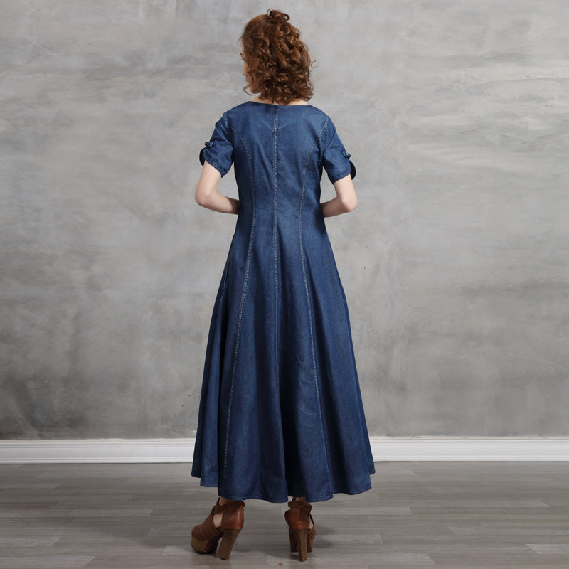 Woman wearing a blue dress standing against a gray wall.