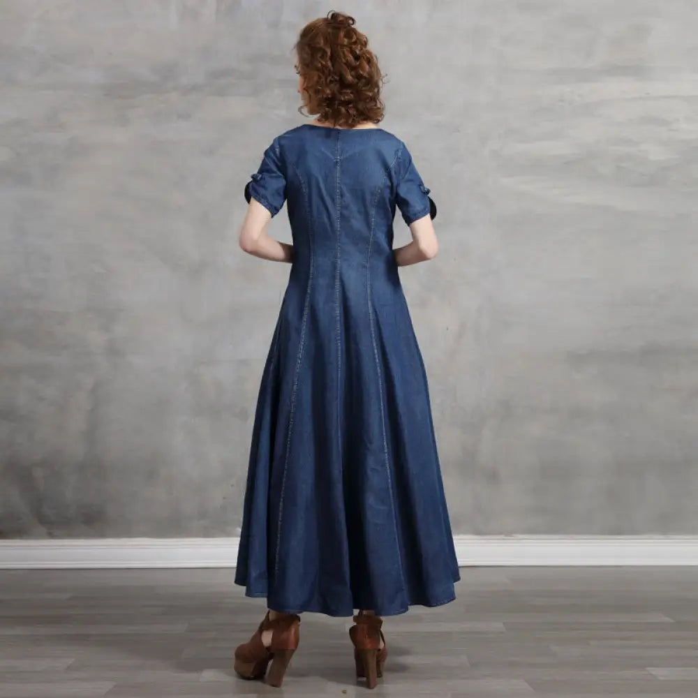 Woman wearing a blue dress standing against a gray wall.