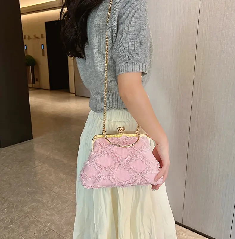 Person holding a pink lace handbag with gold chain strap indoors.