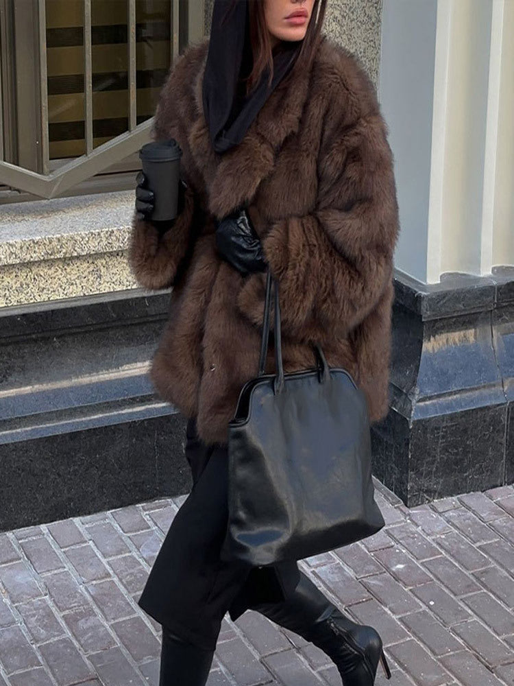 Person wearing a brown fur coat and holding a black handbag on a city street.