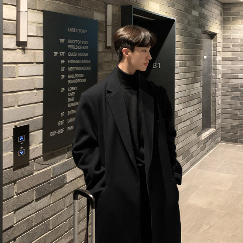 Man in a black coat standing in front of an elevator with a directory on a brick wall.