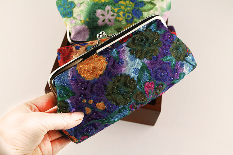 Colorful floral-patterned clutch held by a hand against a neutral background