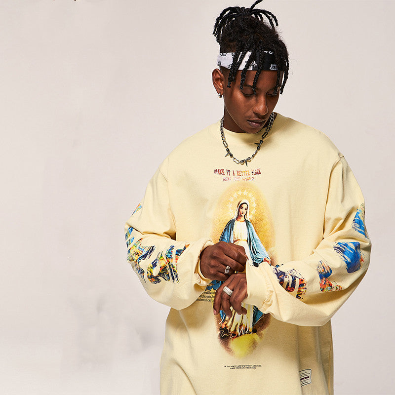 Person wearing a beige sweatshirt with religious-themed graphics on a plain background