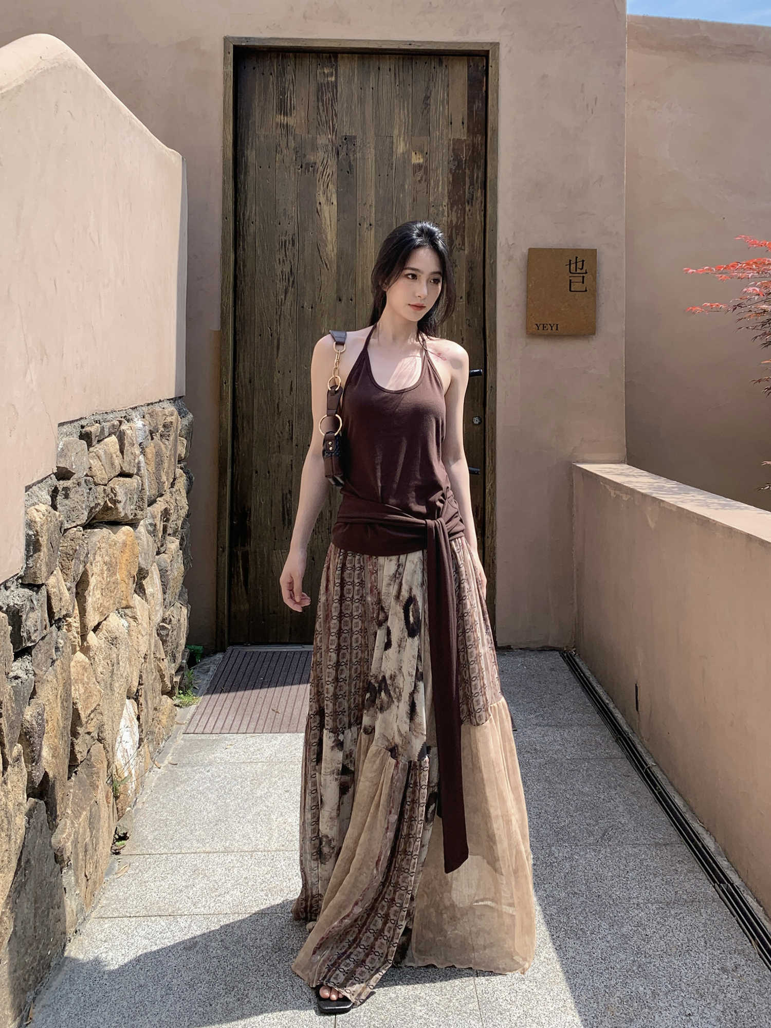 Woman in a long, patterned dress standing in front of a wooden door.