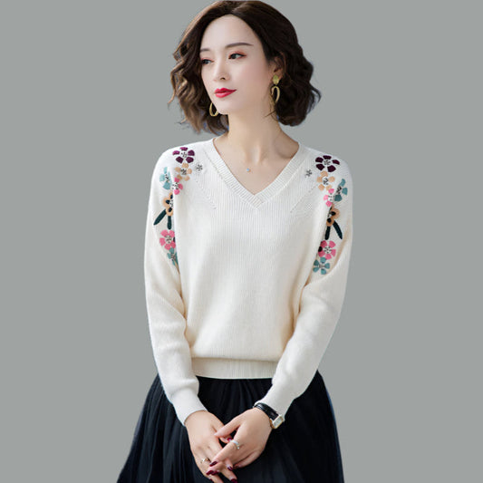 Woman wearing a white sweater with floral embroidery on a gray background