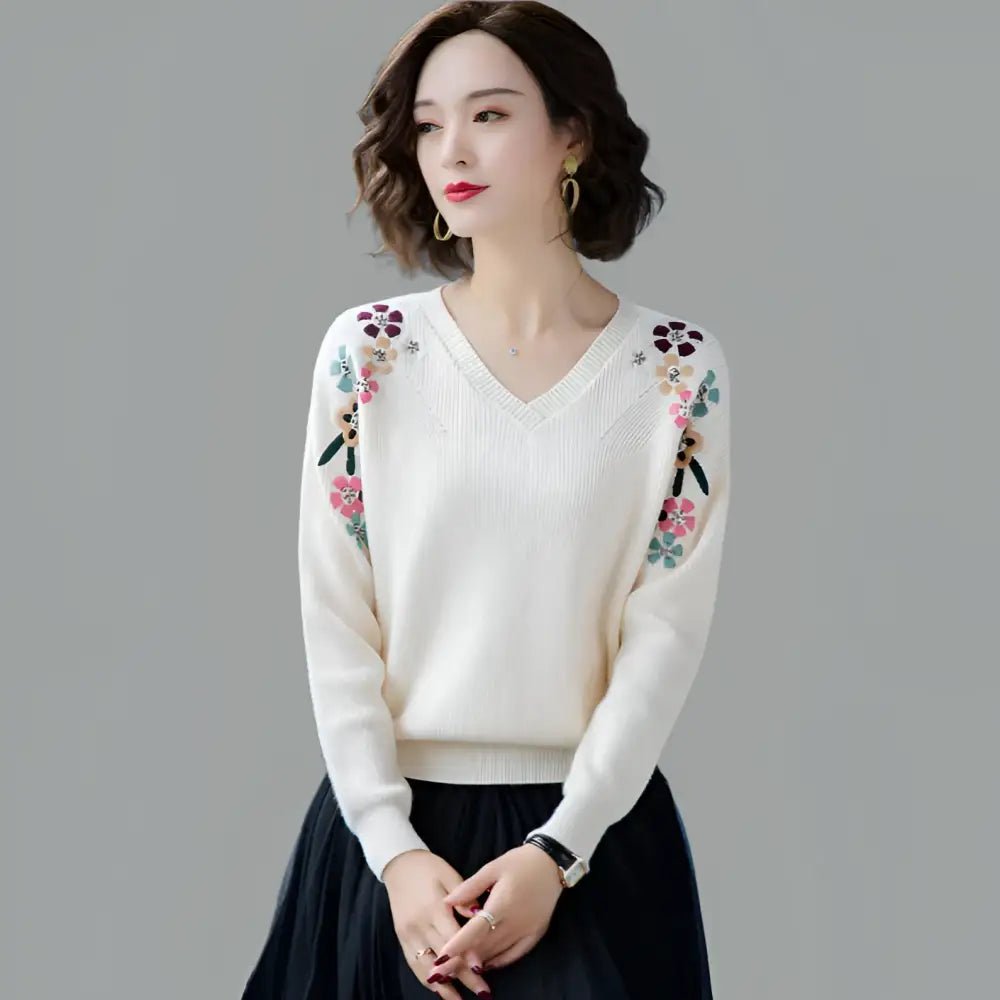 Woman wearing a white sweater with floral embroidery on a gray background