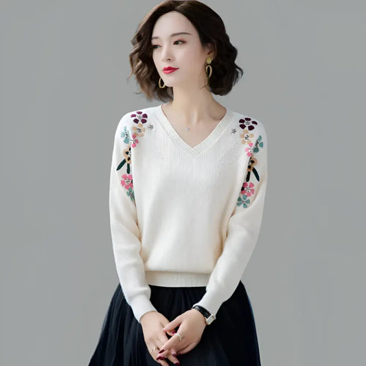 Woman wearing a white sweater with floral embroidery on a gray background