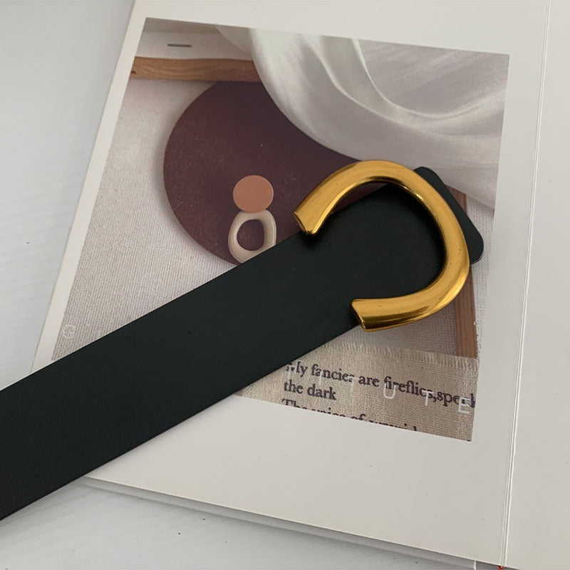 A brown belt with a gold-colored buckle placed on a flat surface, partially lying on a white object which appears to be a piece of paper or fabric.