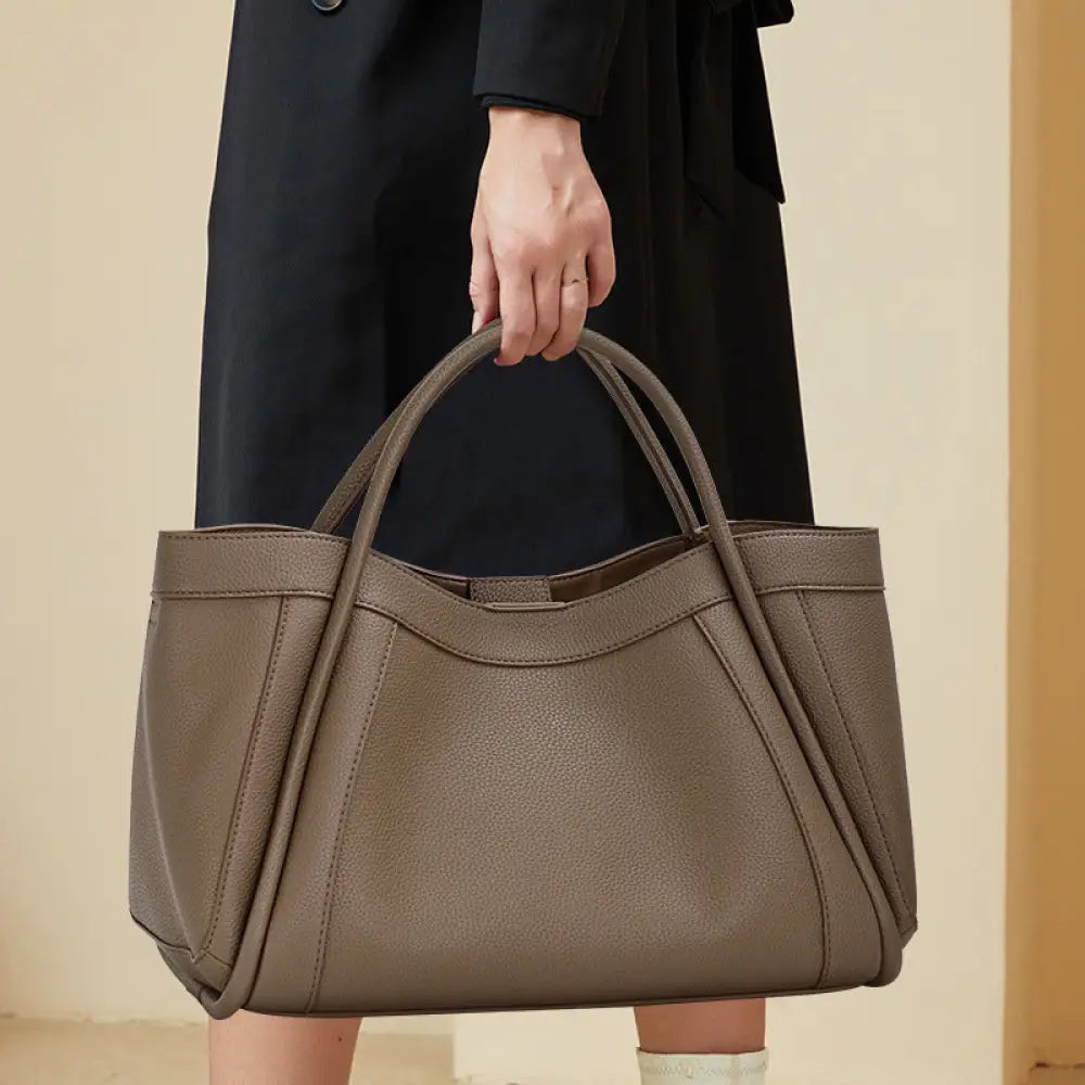 Person holding a brown handbag against a neutral background